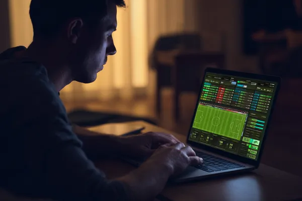 A man focused on his laptop with live stats in the background, highlighting the dedicated sports and gaming features of the KG999 mobile app.