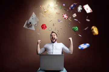 A man celebrating a winning moment on his laptop while gaming symbols float around him, capturing the excitement of KG999 games.