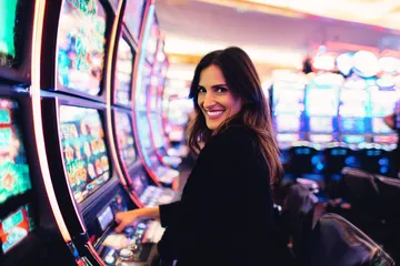 A woman smiling by bright slot machines showing lucky symbols, showcasing the exciting slot offerings at KG999.